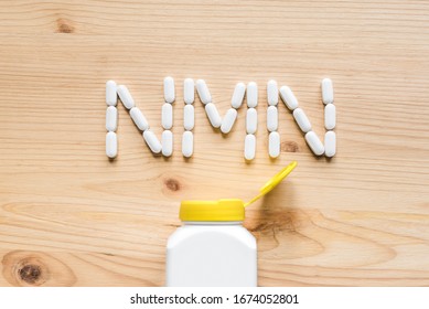 Nicotinamide mononucleotide, niacin, anti adeing vitamin. White pills forming shape to NMN alphabet on wooden background, copy space, top view.