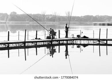 NIEPRUSZEWO, POLAND - JUNE 23, 2016. Two Older Men Fishing From A Lake Pier In The Morning