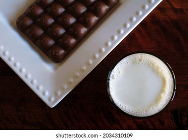 NIGEL, GAUTENGSOUTH AFRICA – SEP 1, 2021: Top Down View Of Glass Of Frothy Milk Next To Slab Of Aero Milk Chocolate On A Square Plate.