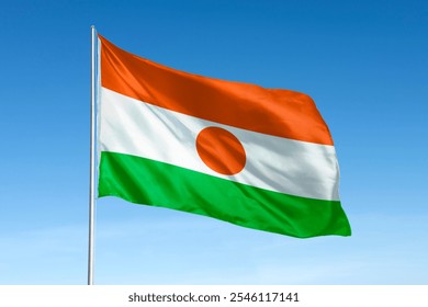 Niger flag waving against a clear blue sky. The flag of Niger features orange, white, and green stripes with an orange circle. National flag of Niger. Niger national flag. - Powered by Shutterstock