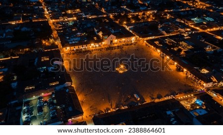 Night aerial view of Villa de Leyva’s main square with church, Boyaca, Colombia. Bustling with people, lit by colorful lights