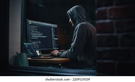 Night Apartment: Evil Greedy Hacker Wearing Hoodie, Breaks into Data Servers, Does DDOS Attack, Phishing Scheme, Malware, Sends Virus. Cyber Security and Crime Concept. View From Outdoors into Window. - Shutterstock ID 2209519339