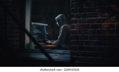 Night Apartment: Evil Male Hacker Wearing Hoodie Breaks Into Data Server Room, DDOS Attack, Phishing Scheme, Malware. Darknet Cyber Crime Concept. View From Outdoors Into Window.