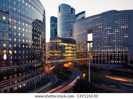 Night architecture. Skyscrapers with glass facade. Modern buildings in Paris business district. Evening dynamic traffic on a street. Business, economy and finances concept.  Copy space for text. Toned