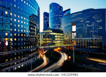 Night architecture - skyscrapers with glass facade. Modern buildings in Paris business district. Evening dynamic traffic on a street. Concept of economics, finances.  Copy space for text. Toned