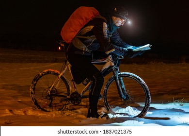 Night Bike Rider Check Track Itinerary In Light Of A Headlight. 16th Of Martch 2016. Prague, Czechia. Lost Path In Snowdrift, Snowflakes Melting On Dark Off Road Tyre. Extreme Bike Orienteering Ra