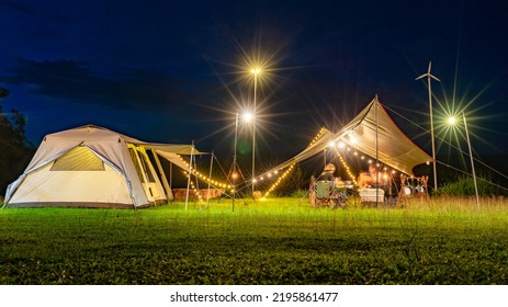 Night Camping Scenes, Long Exposures In Moving Parts Are Blurry.
Night Camping With Tent Accommodation And Relaxation Seats, With Two Young Asian Teenagers Having Dinner Inside The Tent.