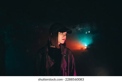 Night cinematic portrait of a beautiful woman in casual clothes standing in the fog at night in red and turquoise light, looking at the camera with a serious face. - Powered by Shutterstock