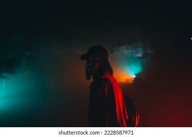 Night cinematic portrait of stylish woman in dark park in colored light in casual clothes, looking at camera, face in shadow. - Powered by Shutterstock