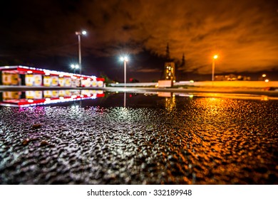 Night City After Rain, Lights Illuminating The Parking Lot Near The Shopping Mall. Wide Angle View Of The Level Of Puddles On The Pavement