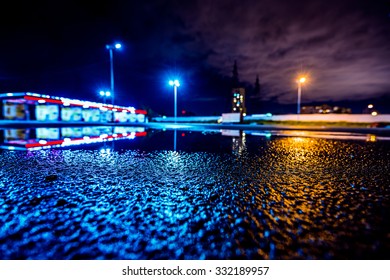 Night City After Rain, Lights Illuminating The Parking Lot Near The Shopping Mall. Wide Angle View Of The Level Of Puddles On The Pavement, Image In The Blue Toning