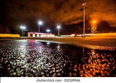 Night City After Rain, Lights Illuminating The Parking Lot Near The Shopping Mall. Wide Angle View Of The Level Of Puddles On The Pavement