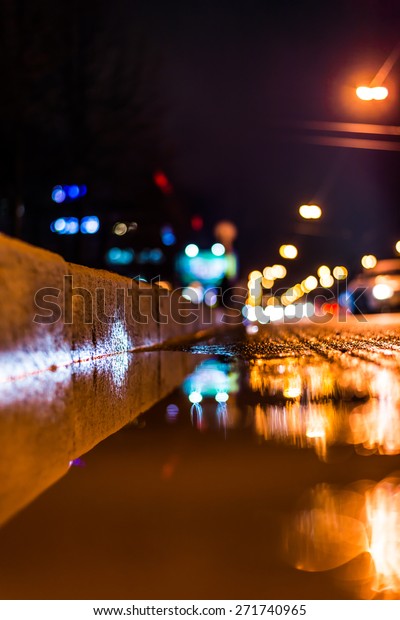 Night city after rain, a reflection of the city at\
night in the water. View of the stream of cars from the roadside at\
the asphalt level