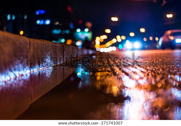 Night city after rain, a reflection of the city at\
night in the water. View of the driving cars from the roadside at\
the asphalt level