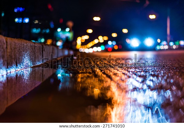 Night city after rain, a reflection of the city at\
night in the water. View of the driving car from the roadside at\
the asphalt level