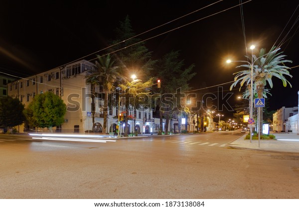 Night\
city lit intersection, along the road grow trees and palm trees, on\
the first floors of buildings are shops and\
cafes