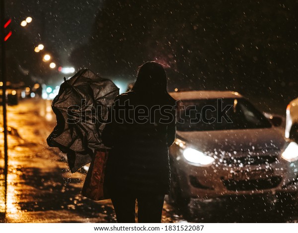 Night city street during the rain. Silhouette
of a woman at night in the light of headlights of cars. The woman
goes to the taxi car and folds the umbrella. Raindrops flow down
from the umbrella.