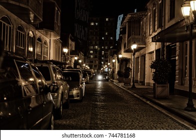 Night City Street. Road With Paving Stone, Lit By Street Lamps With Parked Cars. No People.