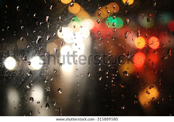 Night city through wet window. Raindrops\
on the glass, on a background of the night\
city.