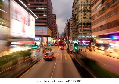 Night Cityscape Of A Busy Street Flanked By Office Towers And Colorful Neon Signs At Dusk In Vibrant Kowloon Downtown (Mong Kok), Hong Kong, China, Asia ( A Dynamic View From A Fast Moving Car )