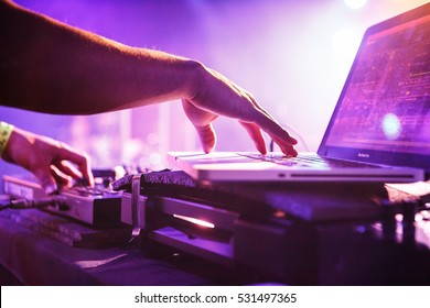 Night Club Dj Playing Music On Stage. Concert Disc Jockey Mixing Electronic Musical Tracks With Midi Controller And Apple Macbook Pro Laptop In Bright Stage Lights. USA - 1 MAY,2022