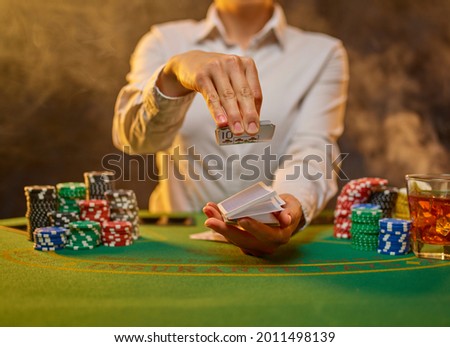 Night club. Gambling. Leisure, hobby. There are many colored chips on the green gambling table. The croupier holds playing cards in his hands. There is an empty space for your lettering.