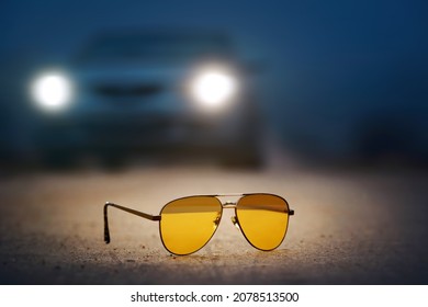 Night Driving Glasses With Yellow Lens And Antireflective Coating For Safely Driving At Night And Fog, Car With Headlights On Background. Selective Focus. Drive Lenses Protect Eyes From Being Blinded