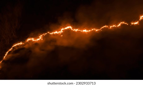 Night fire in the forest with fire and smoke.Epic aerial photo of a smoking wild flame.A blazing,glowing fire at night.Forest fires.Dry grass is burning. climate change,ecology.Line fire in the dark. - Shutterstock ID 2302933713