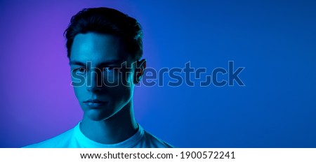 Night. Handsome caucasian man's portrait isolated on purple studio background in neon, monochrome. Beautiful male model. Concept of human emotions, facial expression, sales, ad, fashion and beauty