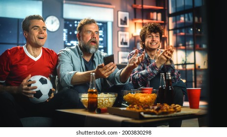 Night At Home: Three Soccer Fans Sitting On A Couch Watch Game On TV, Use Smartphone App To Online Bet, Celebrate Victory When Sports Team Wins. Friends Cheer Eat Snacks, Watch Football Play.