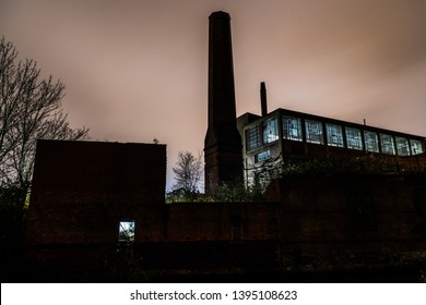 Night Image Of An Old Abandoned Factory With Long Exposure Clouds And Reflected City Light. 