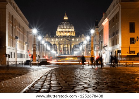 Night Image of Saint Peter's Basilica In Vatican City, Near Rome, Italy With Cobblestones and Shadows Of People And A Crossing Bus, Cars.