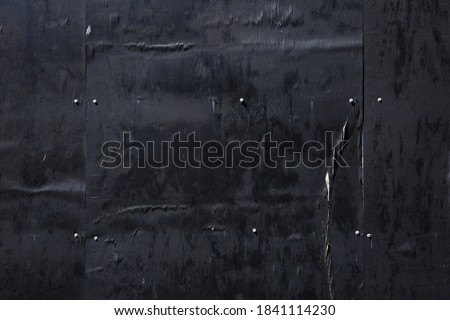 Night image of textures on a wall of black painted weathered plywood on a building worksite fence.