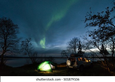 Night Landscape With Illuminated Tent And 4wd Car, Polar (northern) Lights And Lake In The Background. Summer Camping. Tourism. 