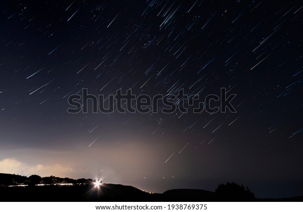Night landscape with star trails. Lights on the\
asphalt, at night on a mountain road, cars on the road leaving\
behind a trail of light.
