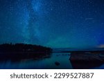 night landscape with a starry sky and the milky way with stars and constellations over the water of a lake with stones