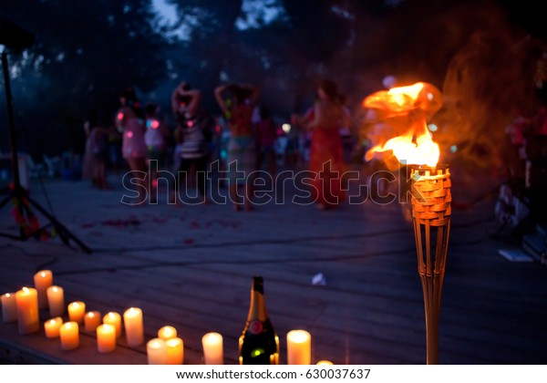 night lit torch on the beach near the water,\
people in the background