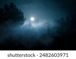 Night mysterious landscape in cold tones - silhouettes of the forest trees under the full moonlight in a cloud of fog. Halloween background.