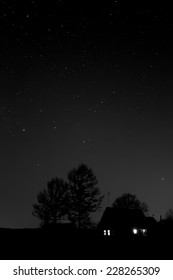 Night on the edge of the village. Dark night in the village. Black-and-white image. The lonely house on the edge of the village under the stellar sky. Pure starlit night over the village. 
