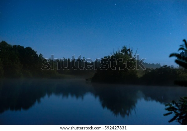Night on the lake with dark blue water and stars on\
the sky