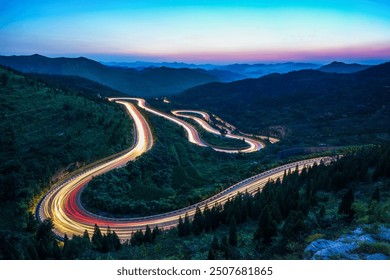 At night, on the winding mountain road, the car lights form a long stream of light - Powered by Shutterstock