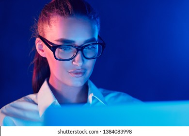 Night Online Work. Woman in glasses using laptop in colorful neon lights