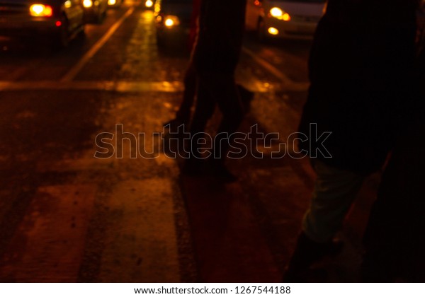 At night, people walk along a pedestrian\
crossing with a reflective car\
headlight.