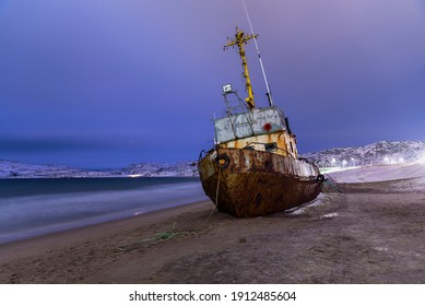 Night Photo Of Fishing Boat Lying On Its Side, Washed Up By A Storm On The Shore Of The Barents Sea, The Kola Peninsula, Teriberka, Russia