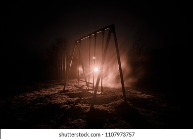 Night photo of metal swing standing outdoor at night time with fog and surreal toned light on background. Nobody there. Lonelyness concept