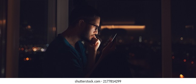 Night portrait of serious man using smartphone near window. Panoramic banner. - Powered by Shutterstock