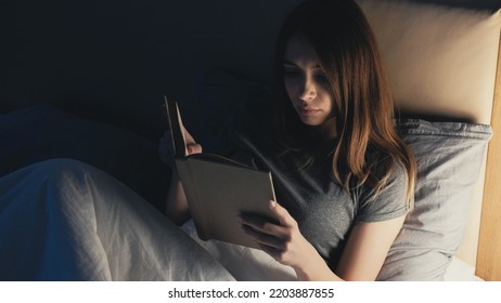 Night Reading. Home Leisure. Rest Time. Relaxed Woman Lying In Bed With Interesting Book Turning Off Light For Sleep In Dark Room Interior.