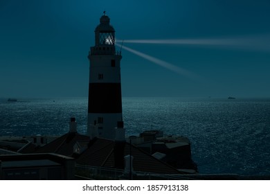 At night at the red and white trinity lighthouse on the British territory of Gibraltar. The moonlight illuminates the Strait of Gibraltar with some ships.