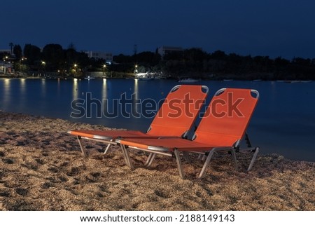 Night sandy beach with two bright beach longchairs against dark blue sky and calm water, Crete, Greece
