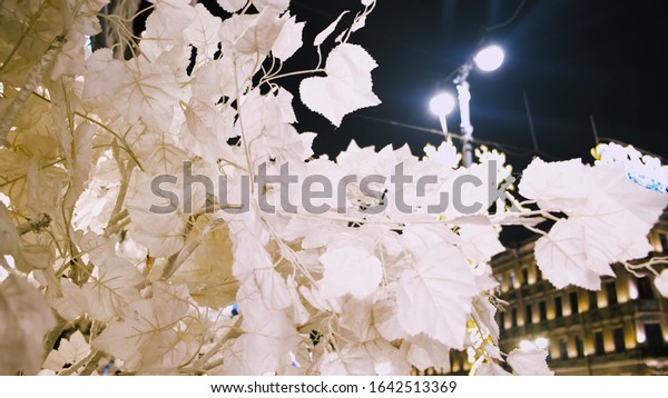 Night scene with\
beautiful white leaves of artificial tree in the street of a big\
city. Concept. Close up of white tender leaves swaying in the wind\
on black sky background.